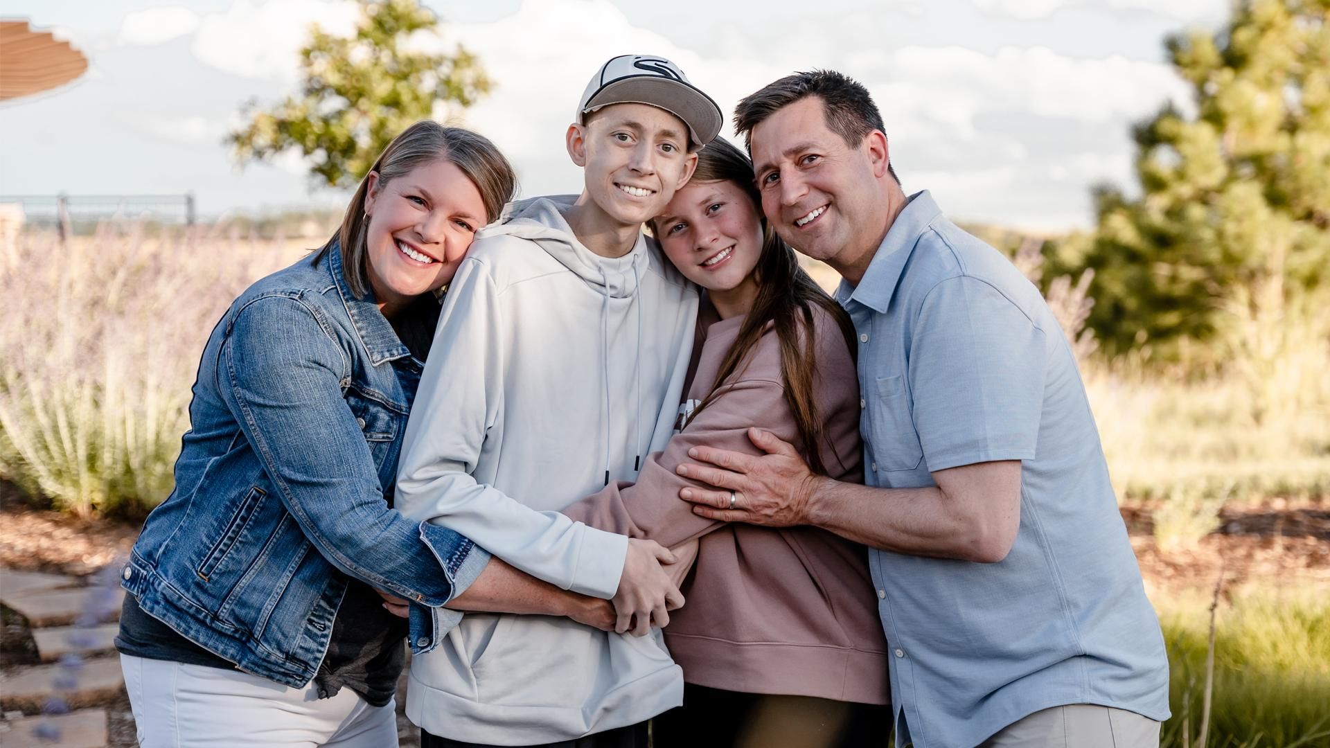 A mother, son, daughter and father have their arms around one another while smiling at the camera.