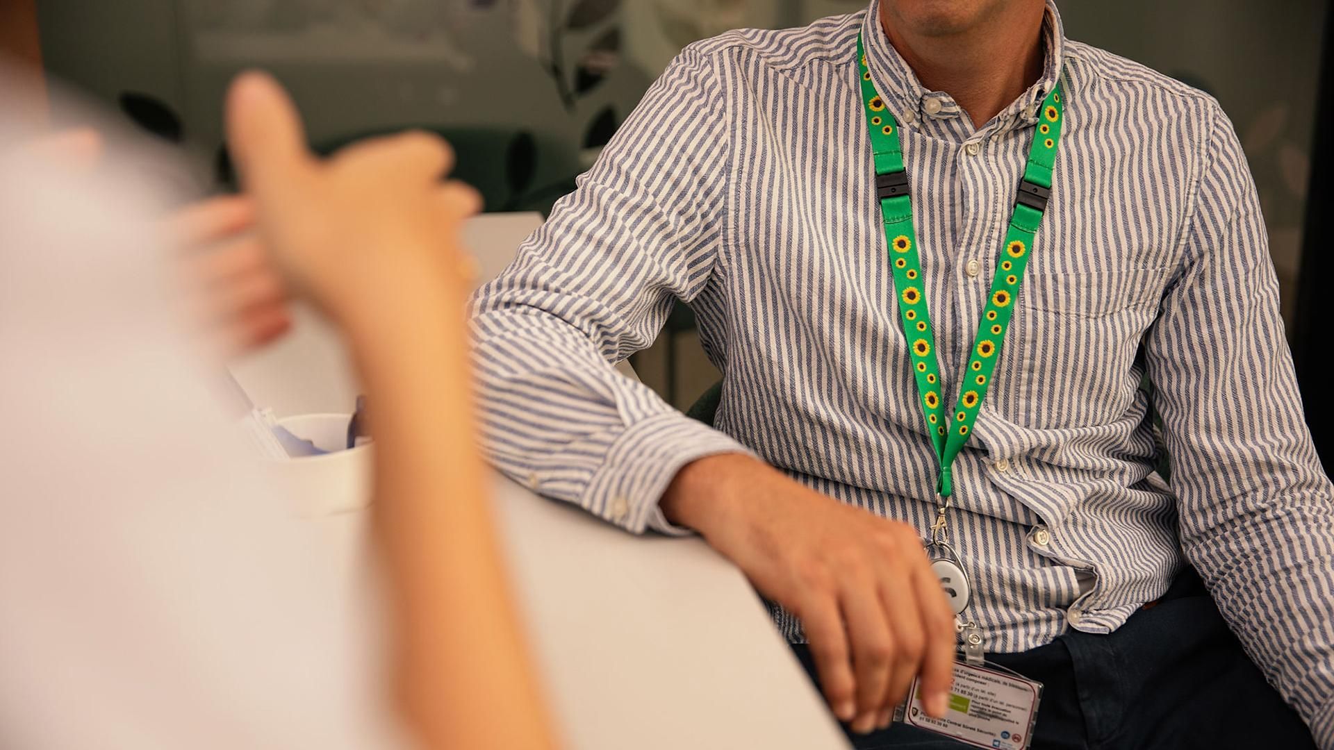 Close-up of the torso and hands of a patient with an invisible disability, wearing a sunflower lanyard to discreetly signal their need for assistance or attention, while engaged in conversation with a healthcare professional.