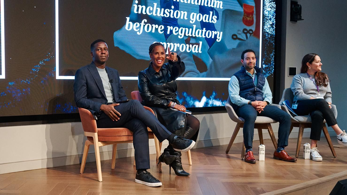 Six people participate in a panel discussion about inclusion in clinical trials, with one speaker standing and addressing the audience.