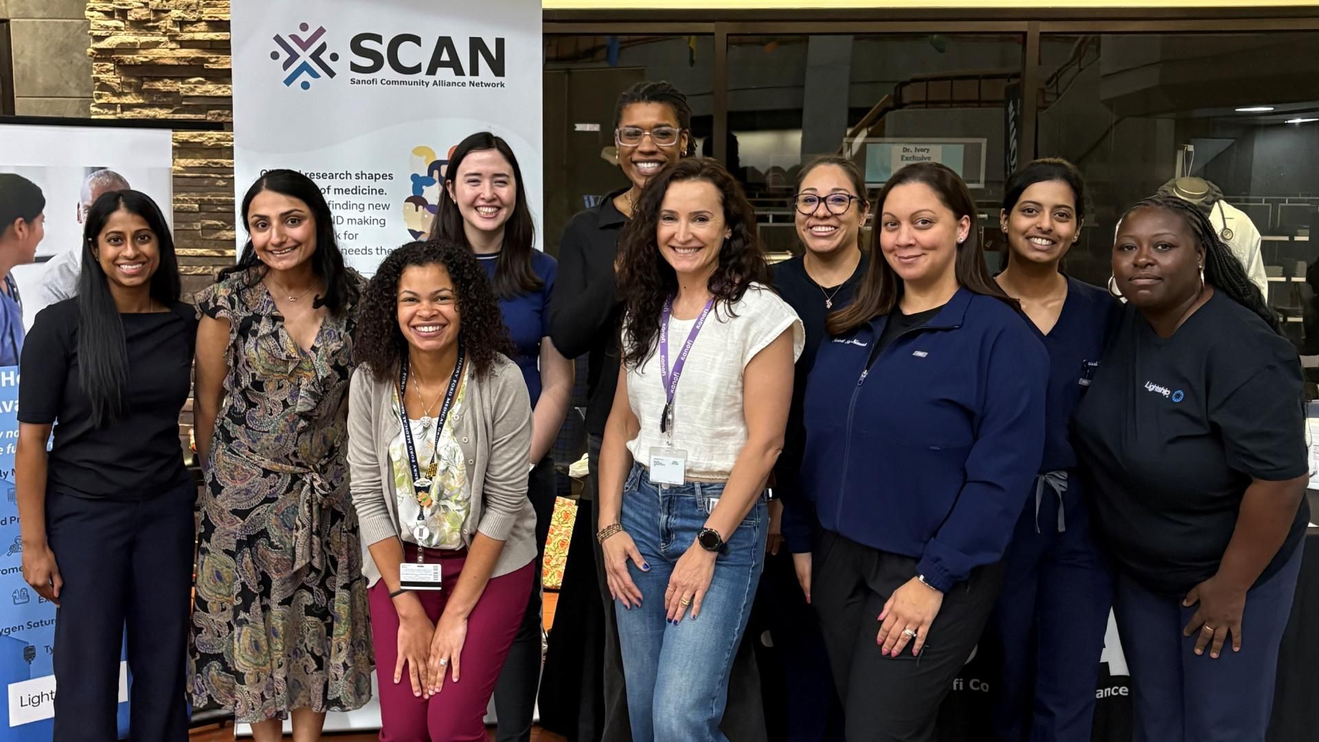 Image of Sanofi Colleagues standing at the Detroit Asthma Fair in front of a Sanofi Community Alliance Network (SCAN) booth banner.