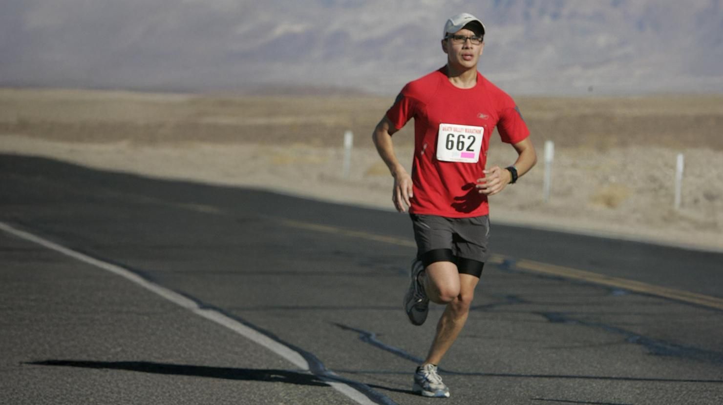 Patient living with Hemophilia A running a half marathon on a desert road. He is wearing a red t-shirt and dark grey shorts and has the race number 662 on his shirt front. 