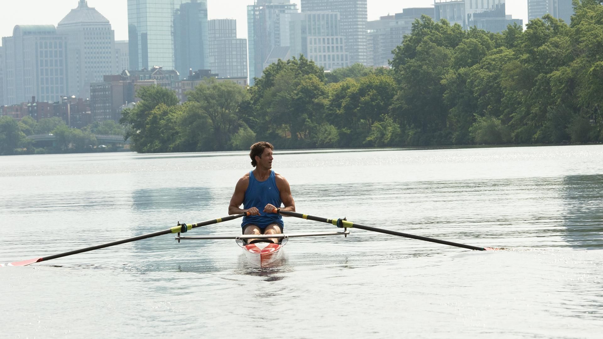 Chris Liwski, rowing a single scull on the Charles River in Boston overlooked by the city.