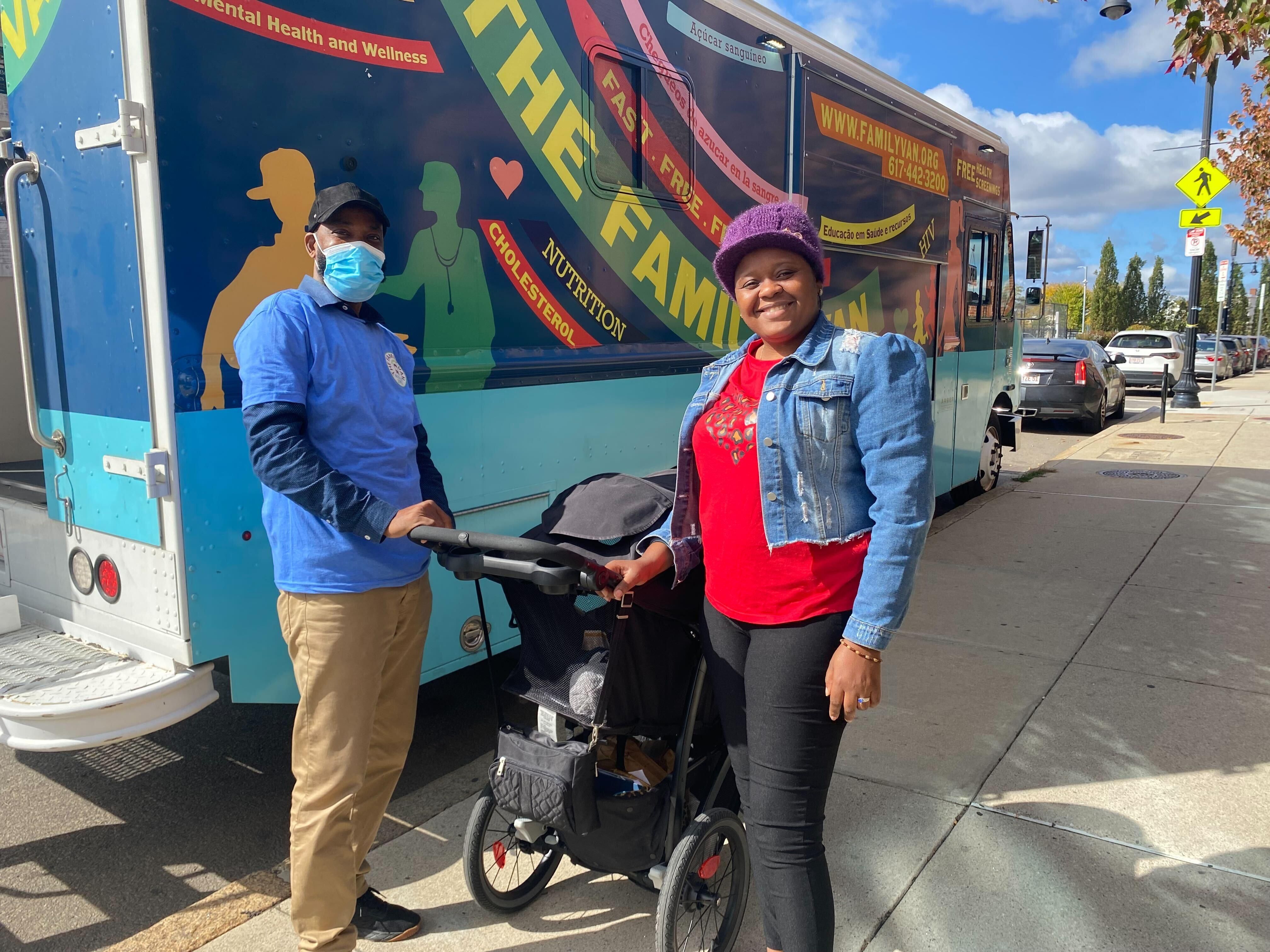 Two individuals stand together on a sidewalk holding a stroller in front of The Family Van, a mobile health unit offering nutrition, cholesterol, and mental health and wellness services.