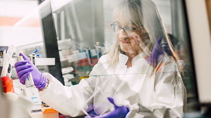 Christine Dureuil Sizaire working in a lab wearing safety purple safety gloves and a lab coat.