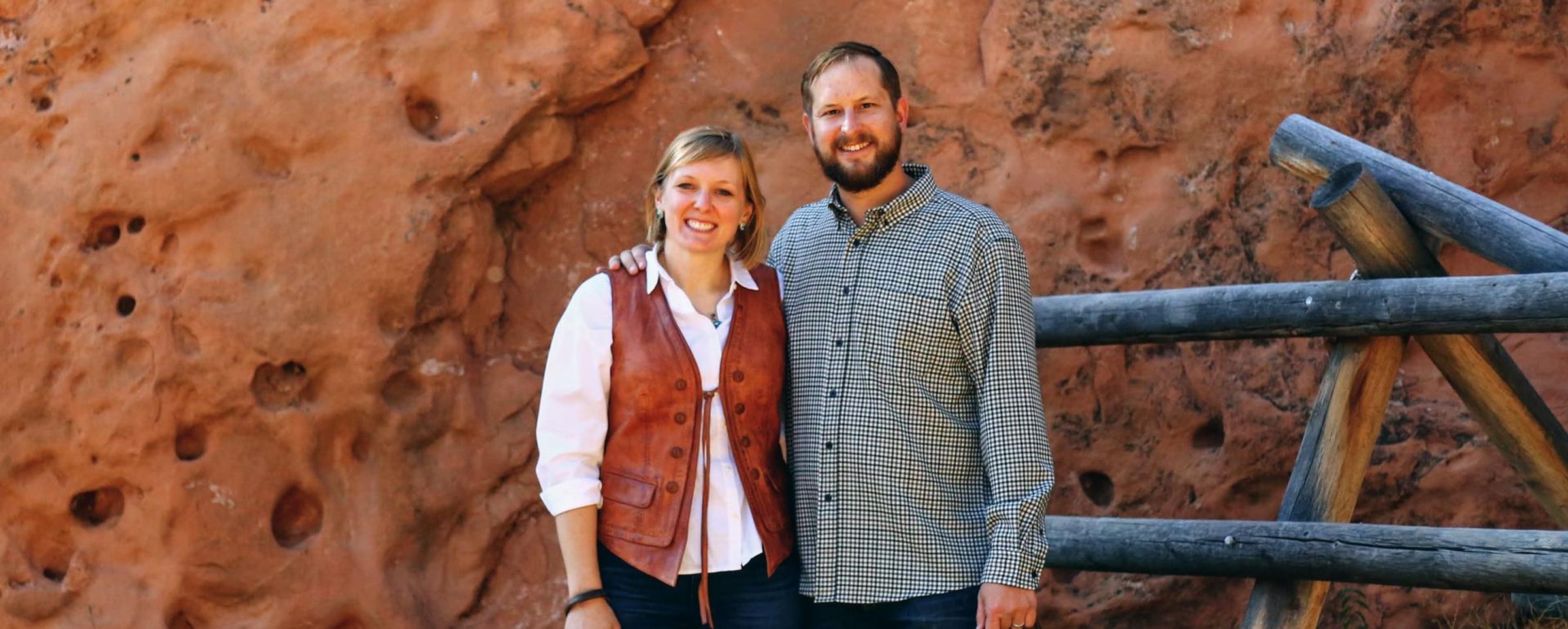 Melanie Stutts stands with her arm around her husband against a stone wall backdrop in Arizona.
