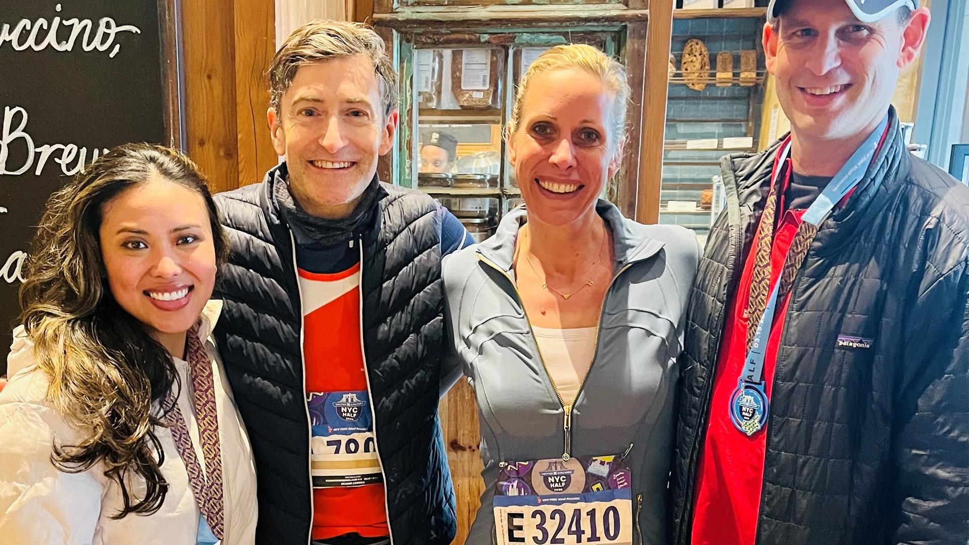 Four Sanofi Transplant Team employees wearing marathon medals and race bibs stand together smiling in a restaurant after completing the 2026 NYC Half Marathon, celebrating their fundraising effort for the National Kidney Foundation.