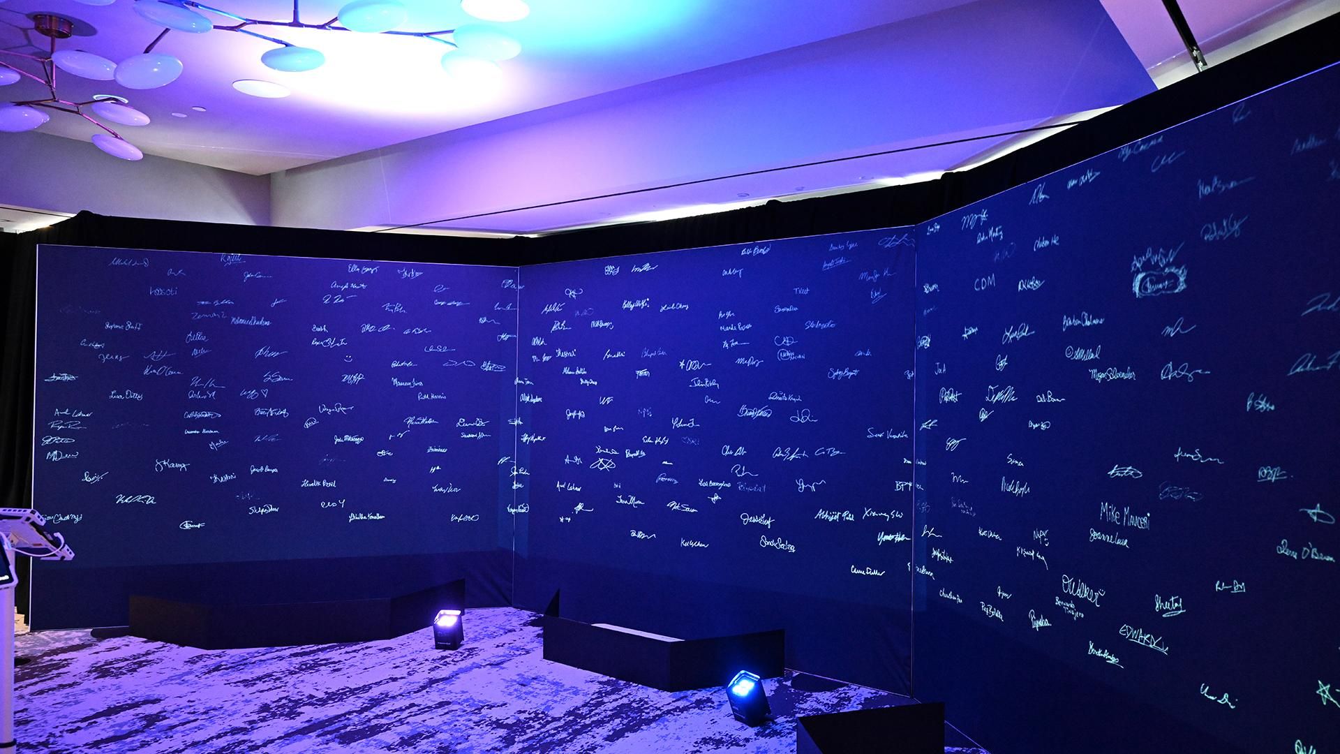 Dark blue illuminated wall covered with hundreds of handwritten white and light blue signatures from Sanofi employees signing the "Declaration of Innovation" during the America 250 immersive employee engagement experience.