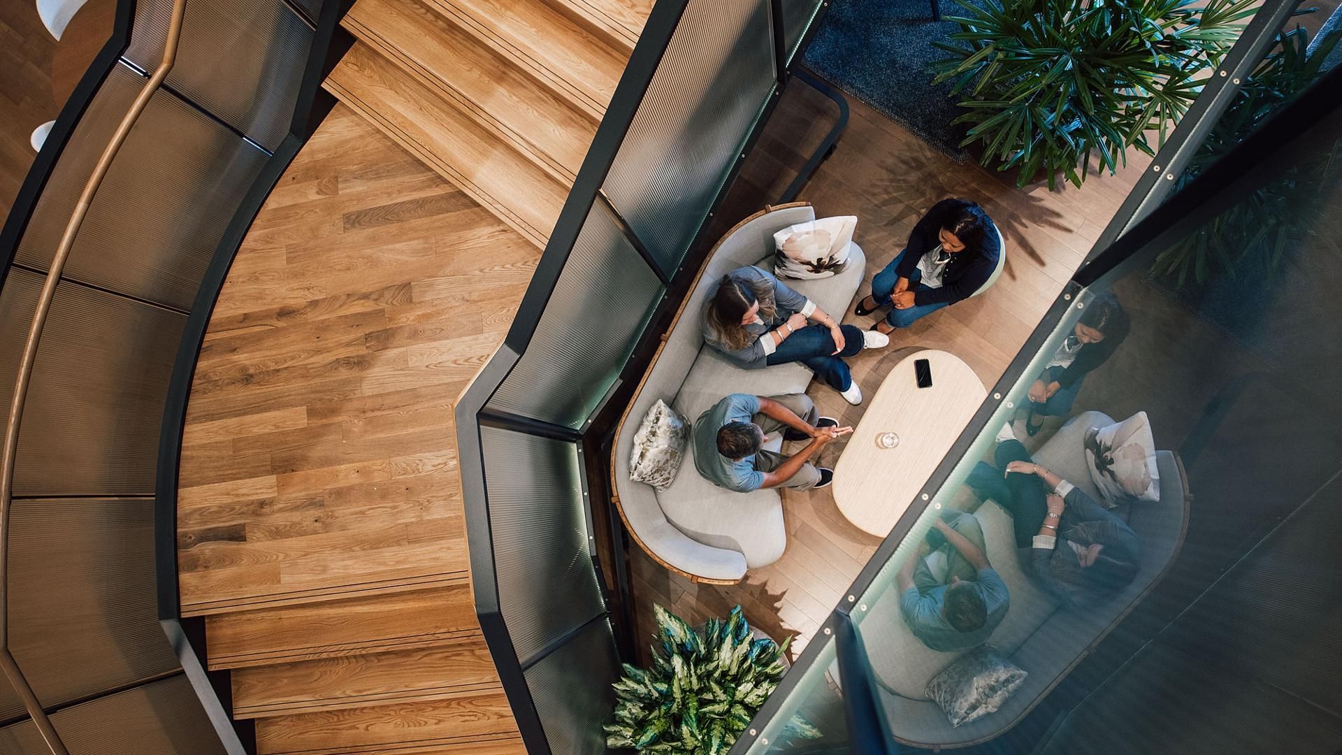 Sanofi employees collaborating in a modern office workspace, gathered around a table near a spiral staircase surrounded by plants.