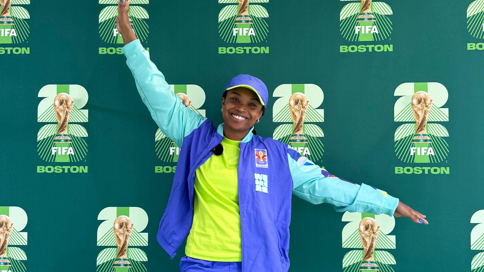 Sanofi Senior Associate Scientist Gigi Abellard stands in front of a World Cup Boston 2026 backdrop, wearing volunteer apparel, representing America 250 civic engagement, Boston community service, and Sanofi employee volunteerism.