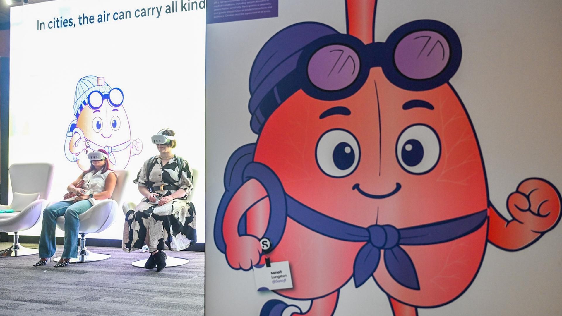 A large illustration of Lungston, a cartoon lung character wearing aviator goggles and a purple scarf with a Sanofi name badge, is displayed on a museum panel during The Air We Share exhibit launch at the Museum of Science in Boston. In the background, visitors sit and explore an interactive exhibit at the museum related to air quality and respiratory health.