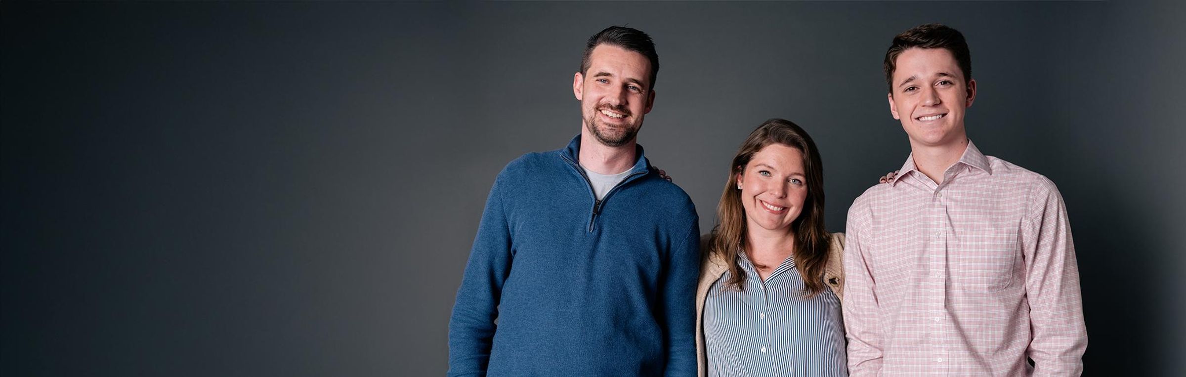 Three diabetes Sanofi Patient Ambassadors, two men and one woman, stand in a row smiling at the camera against a dark grey background.