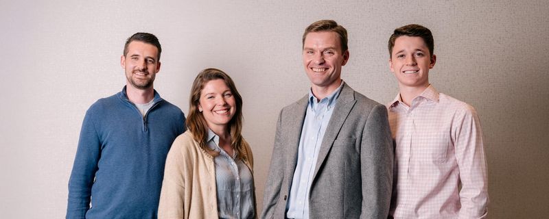 Three diabetes Sanofi Patient Ambassadors, two men and one woman, and a mail doctor, stand in a row smiling at the camera against a light brown background.