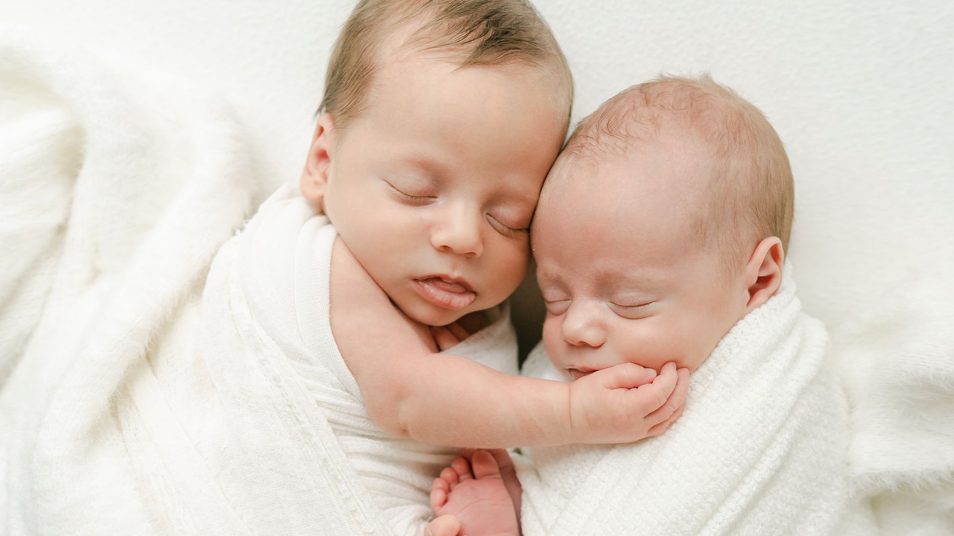 Twin babies with their arms around each other.