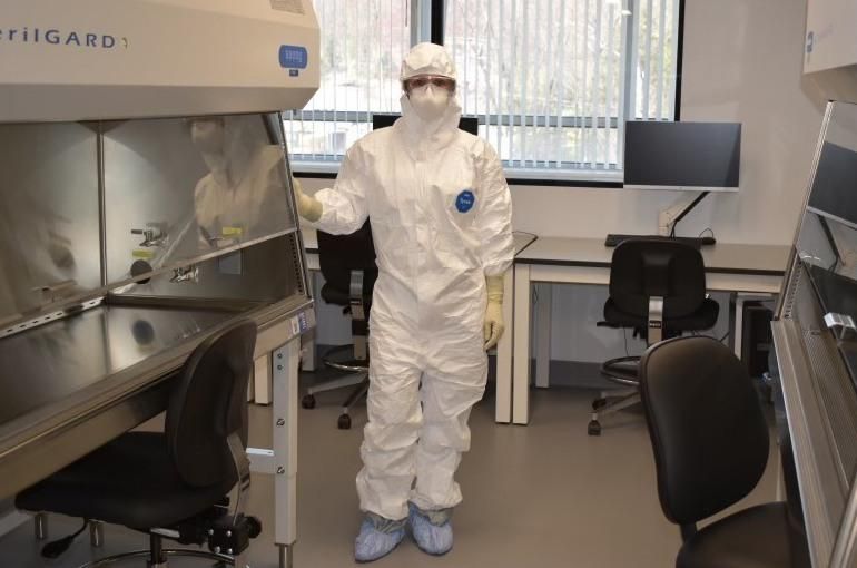 Jennifer Umstead stands inside the BSL3 lab wearing full protective gear: a tyvek suit, gloves, mask, goggles and show covers.