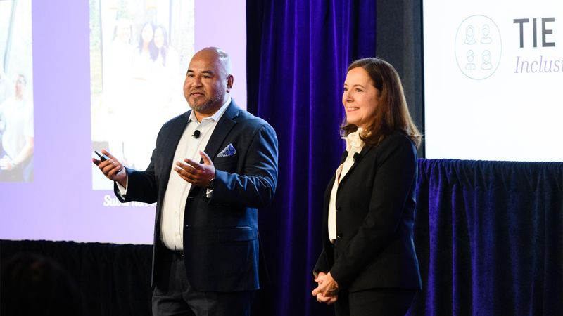 Diana Blankman, Head, Corporate Social Responsibility and Subarna Malakar, Head of Diversity, Equity and Inclusion, North America and Global Specialty Care, People & Culture stand next to each other on stage speaking to an engaged audience