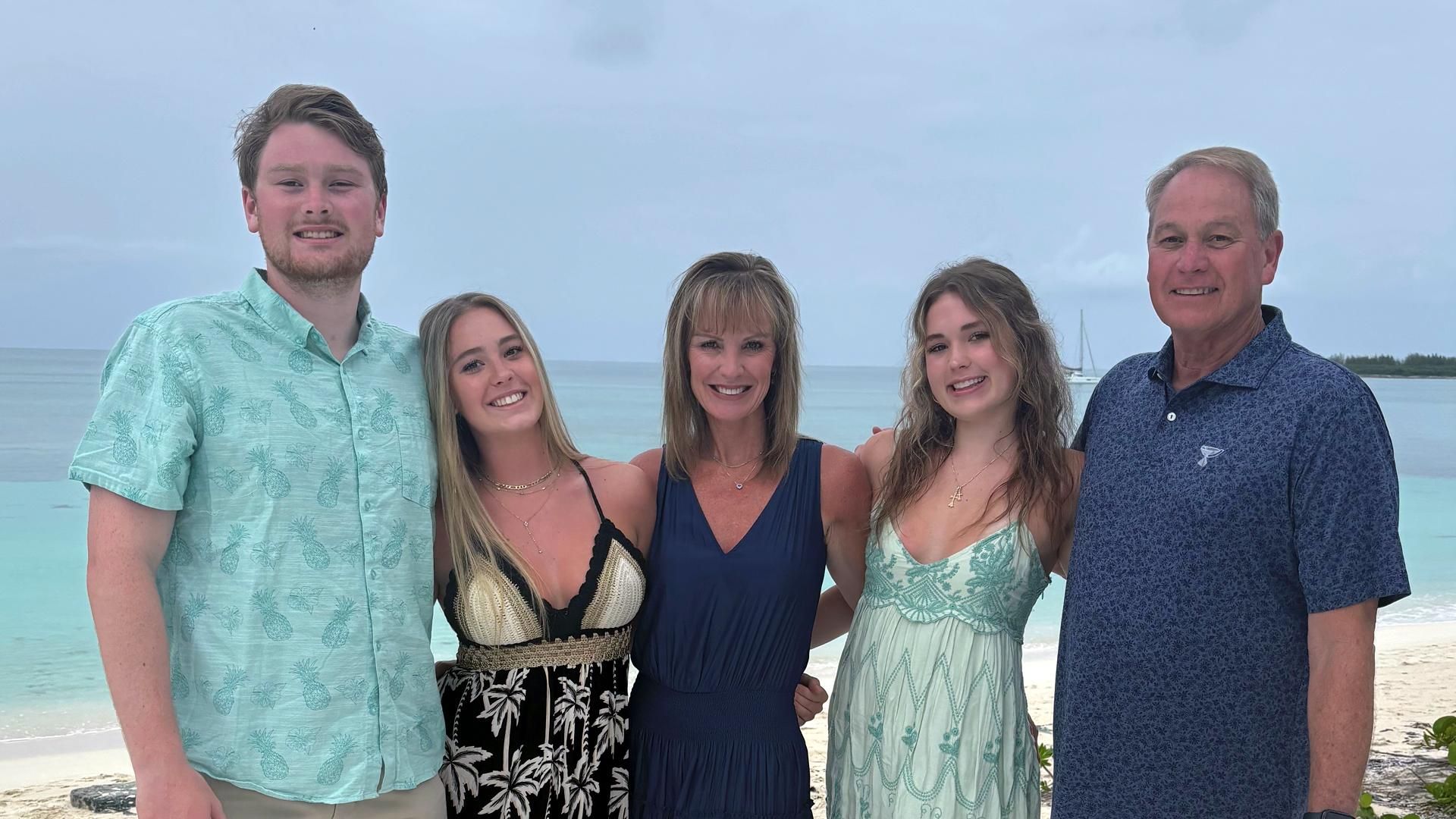 Daye Bexley stands on a balcony off a beach in the middle of her family with her arms around her two daughters, as well as her son and husband on each end.