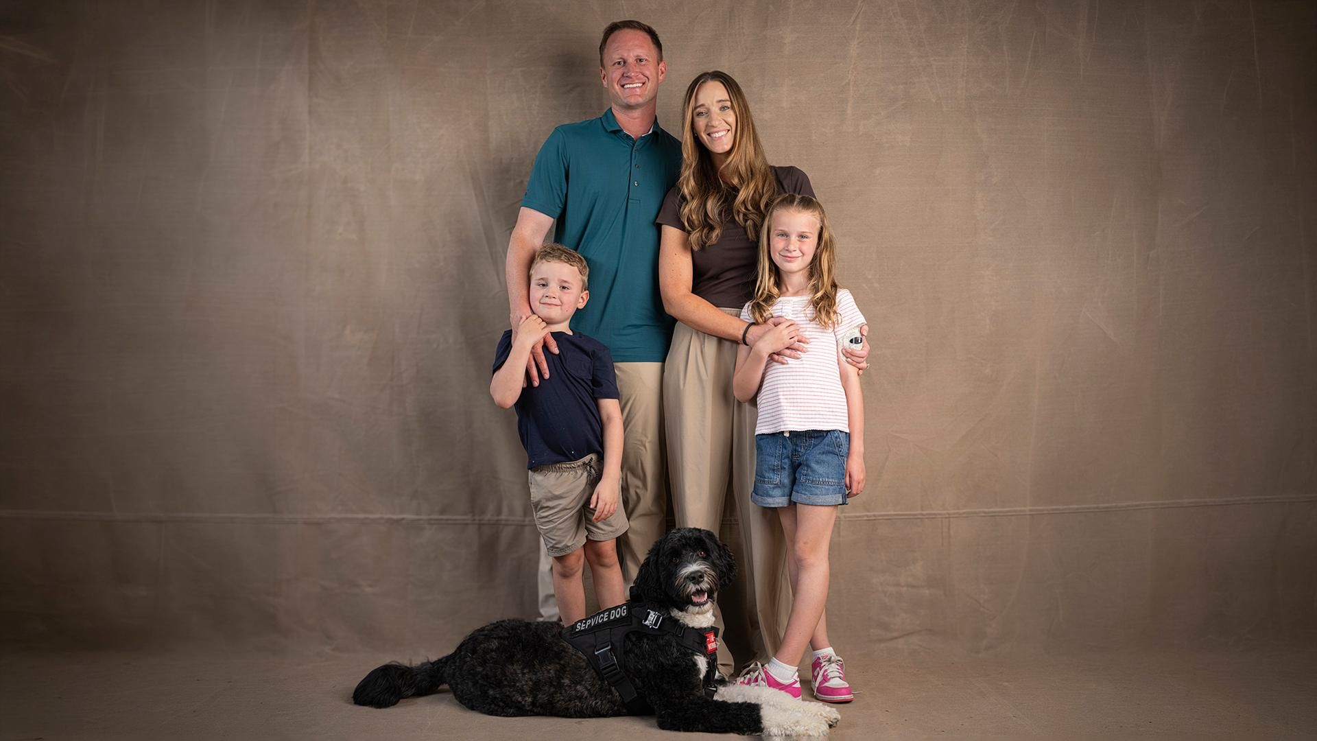 Family of four with dog posing for portrait photo - parents with two children including daughter with type 1 diabetes
