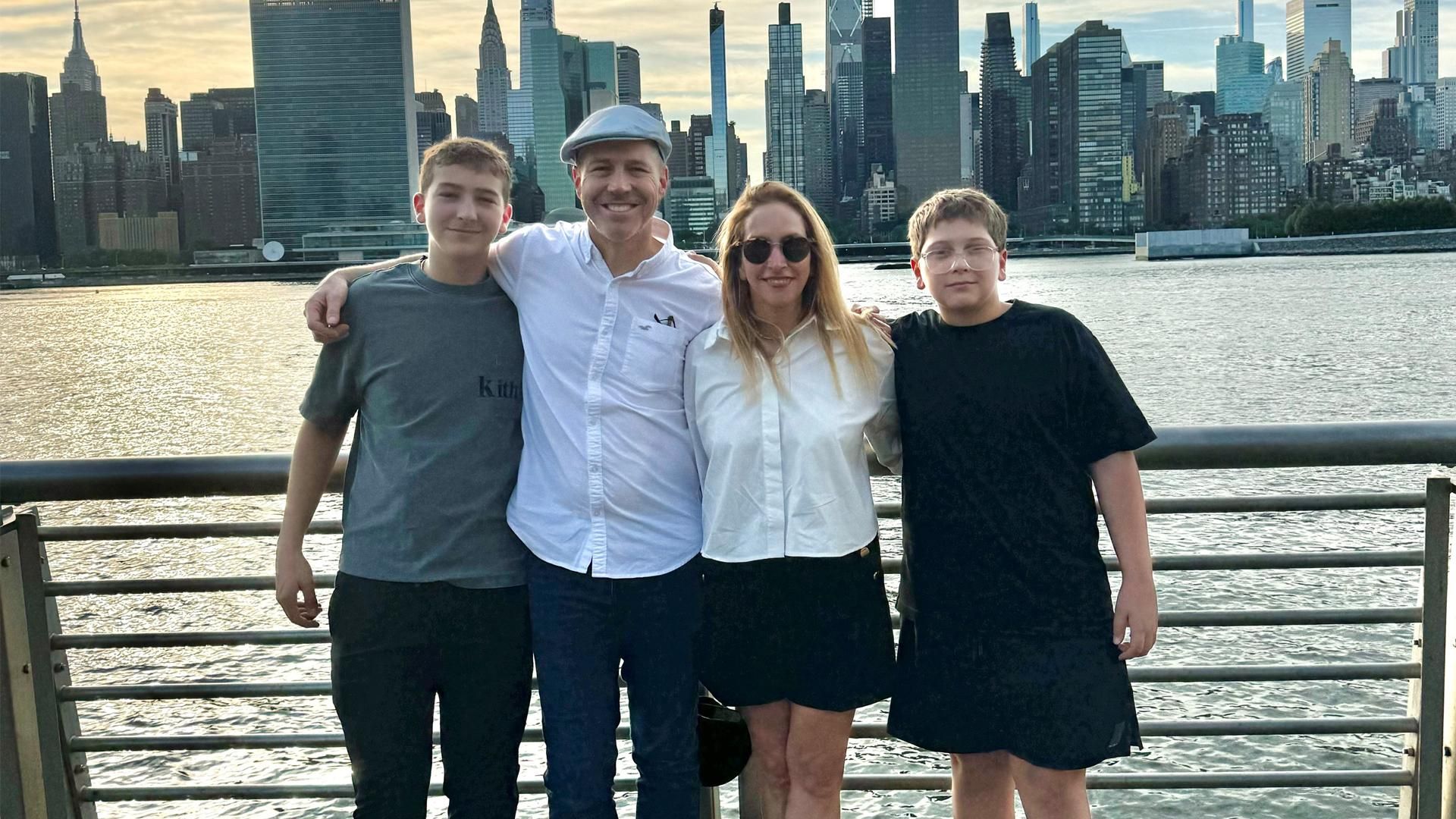 Ayelet, her husband, and two kids pose for a portrait while enjoying an evening on a city pier with the New York City skyline and Hudson River behind them.