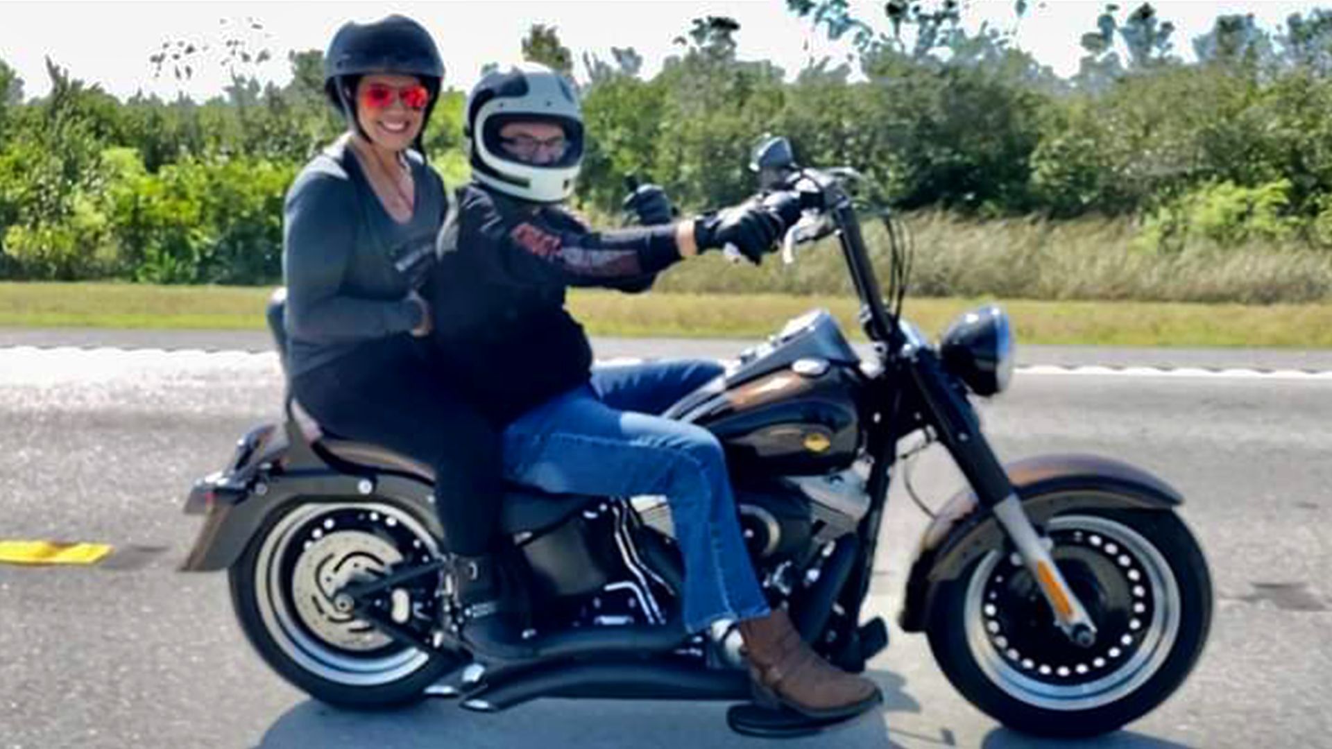 Alex and his wife wearing helmets while smiling for a picture and riding on Alex’s motorcycle.