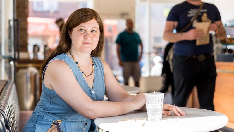 Laura sits in a cafe in a blue dress