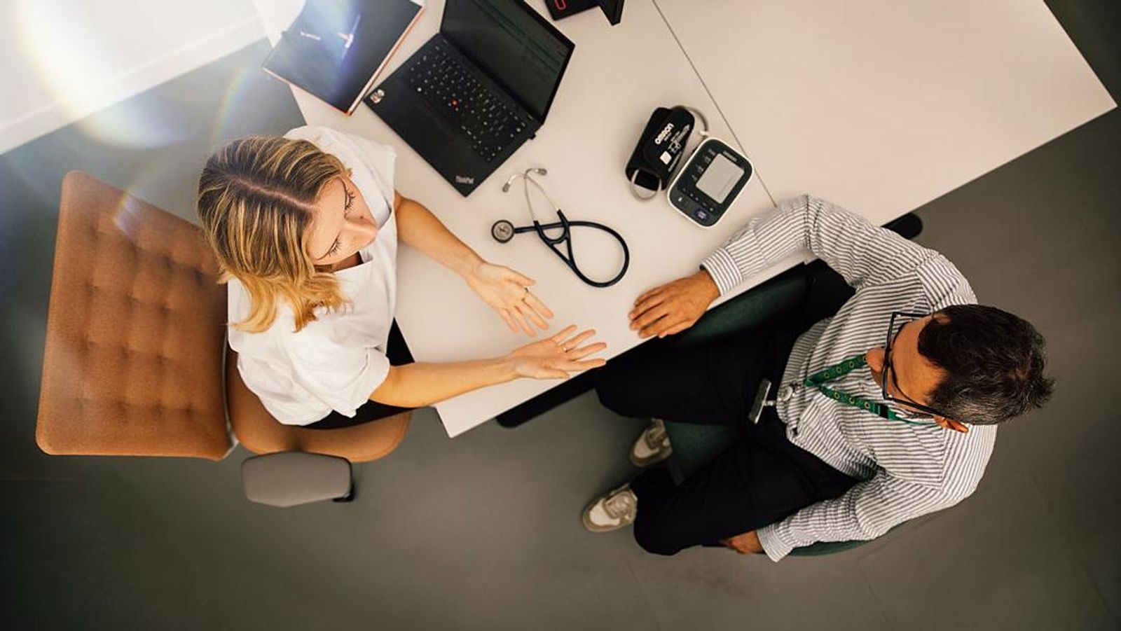An aerial view of a female doctor and a male patient sitting at a table in conversation.