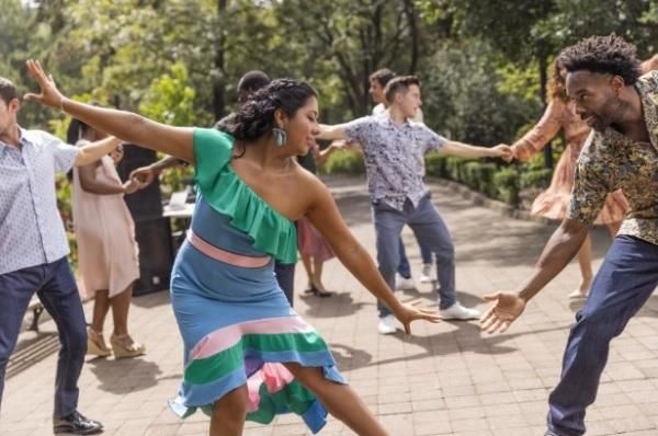 Christal wears a green, pink and blue dress as she dances with a group of diverse people outside.