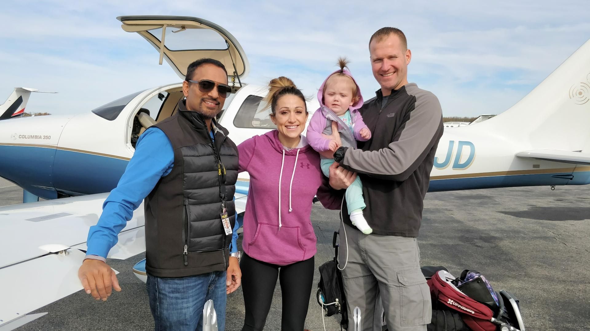 A volunteer pilot stands beside a mother and father holding their baby next to a small aircraft.