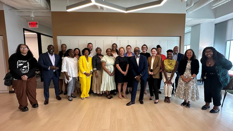 A diverse group of people stand in a line smiling at the camera at AMC Inclusive Dialogue in Cambridge, MA