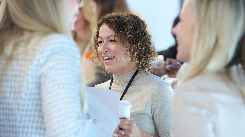Group of people gathered indoors, with a woman in the center of the group holding a paper and displaying a smile.