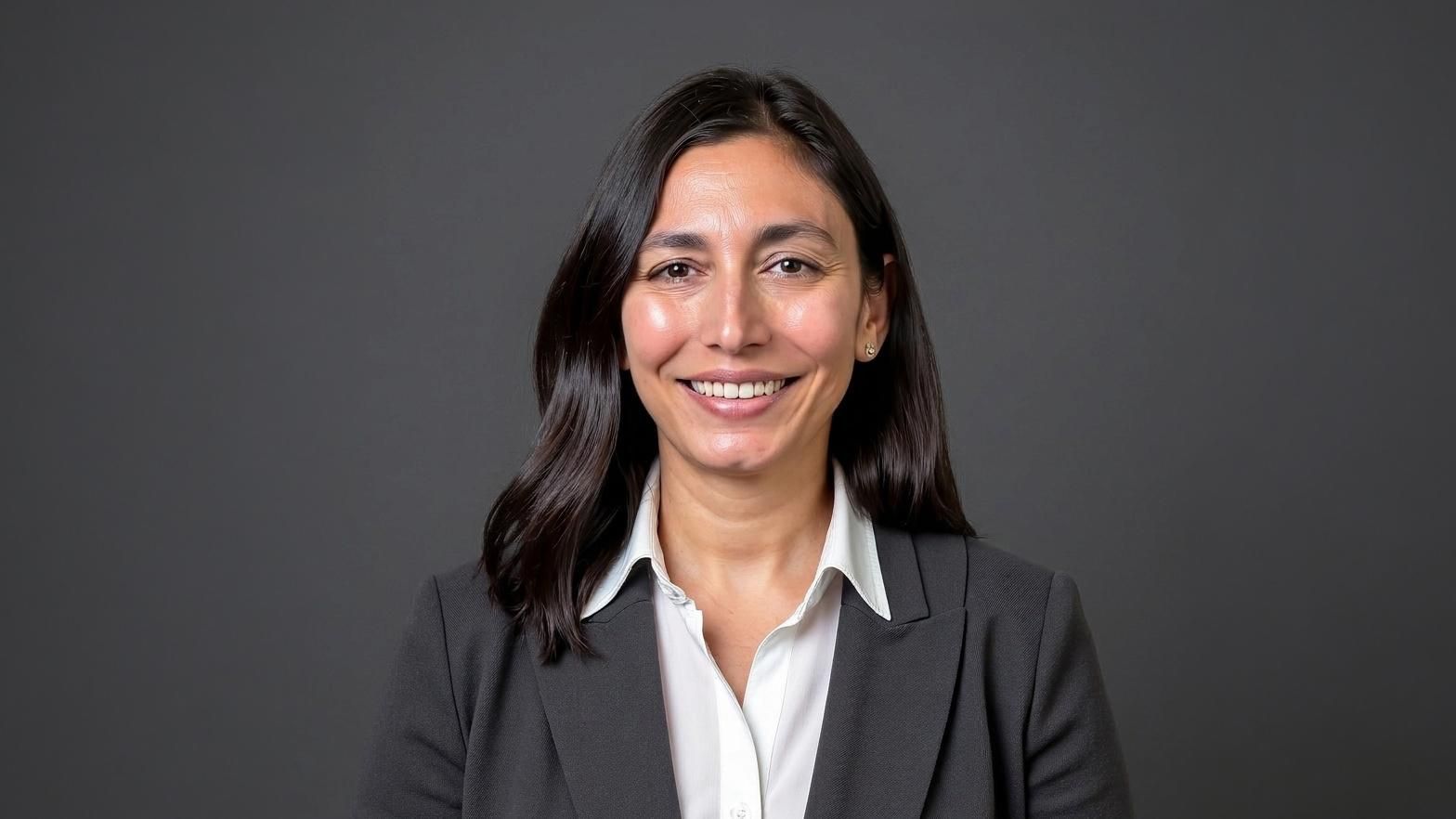Headshot of Sophie with shoulder length brown hair wearing a white shirt and grey blazer against a dark grey background