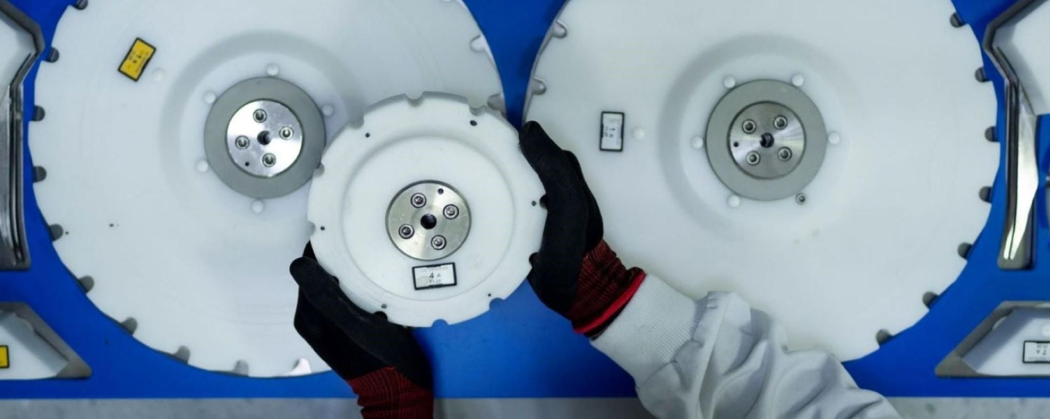 Person in protective gear assembling or inspecting large, circular mechanical components on a blue surface.