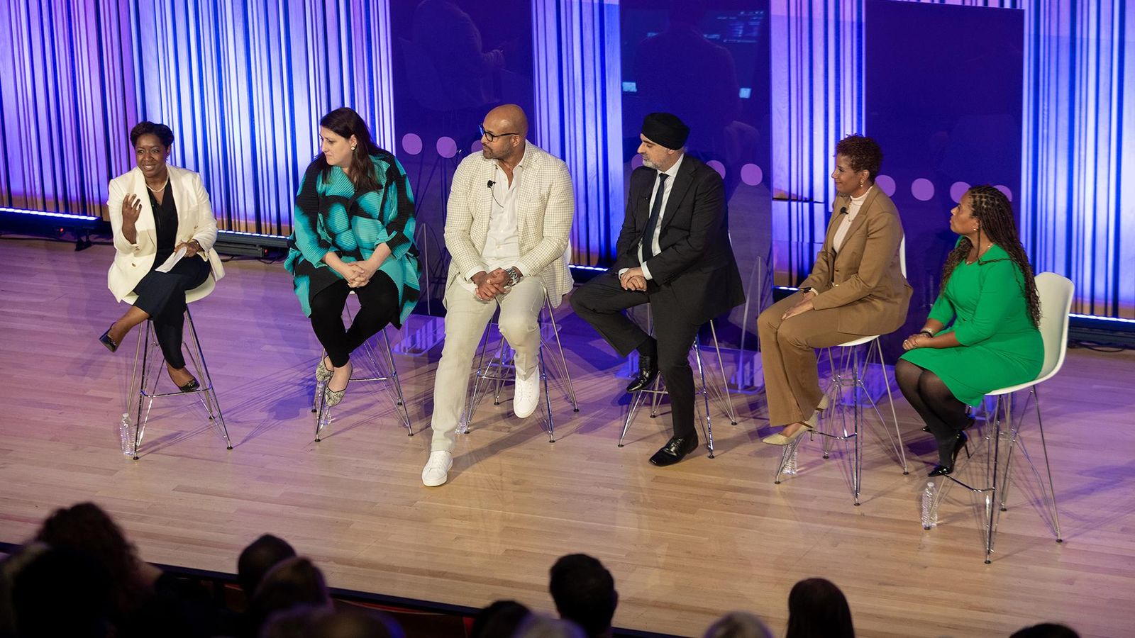 A group of 4 women and 2 men sit on the stage speaking to a crowd.